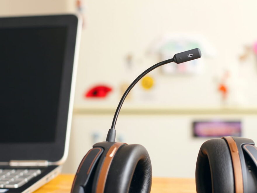 Ein Headset mit Mikrofon auf einem Schreibtisch neben einem Laptop.