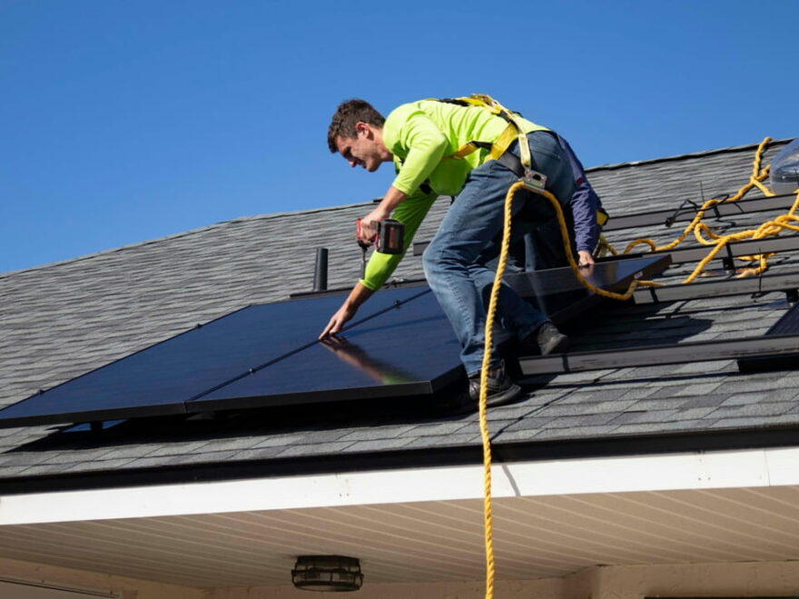 Ein Techniker installiert Solarmodule auf einem Hausdach unter klarem Himmel.