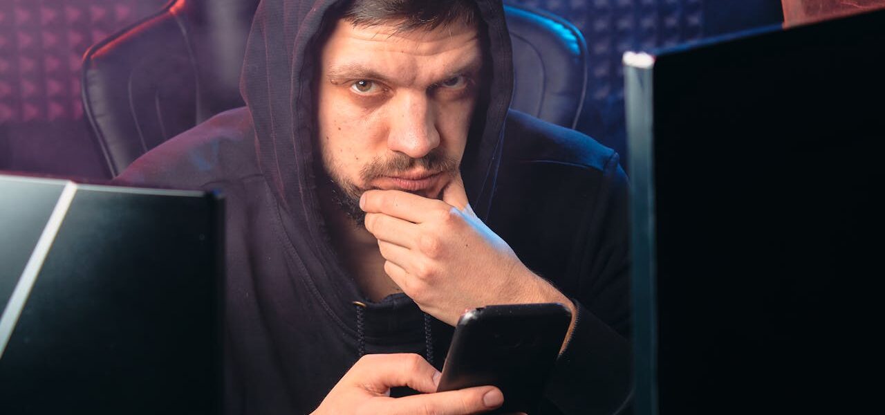 Mann in Kapuzenpulli blickt nachdenklich auf ein Smartphone, symbolisch für digitale Fairness und Datenschutz.