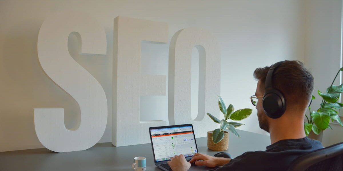 Person arbeitet am Laptop mit SEO-Analyse vor großem SEO-Schriftzug