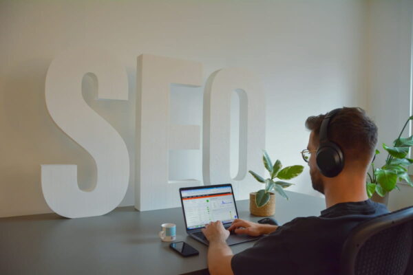 SEO-Arbeit am Laptop vor stilisiertem Schriftzug Person arbeitet am Laptop mit SEO-Analyse vor großem SEO-Schriftzug