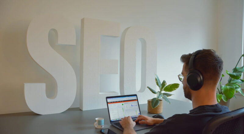 Person arbeitet am Laptop mit SEO-Analyse vor großem SEO-Schriftzug