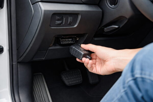OBD2 Anschluss im Auto unter dem Armaturenbrett mit eingestecktem Diagnosegerät